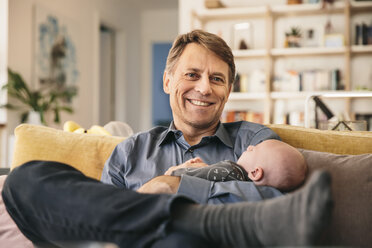Smiling father and his newborn baby sitting on couch at home - MFF03460