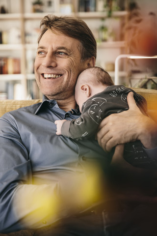 Glücklicher Vater und sein neugeborenes Baby sitzen auf der Couch zu Hause, lizenzfreies Stockfoto