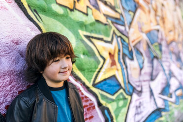 Porträt eines kleinen Jungen, der vor einer Graffiti-Wand steht - MGOF02788