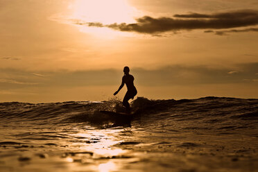 Indonesien, Bali, Silhouette einer Frau beim Surfen im Sonnenuntergang - KNTF00606