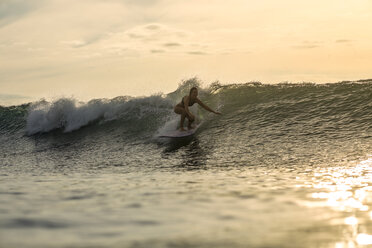 Indonesia, Bali, woman surfing at sunset - KNTF00608