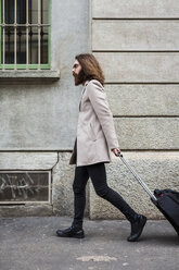 Stylish young man walking with suitcase on pavement - MAUF00927
