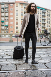 Stilvoller junger Mann mit Koffer beim Überqueren der Straßenbahn - MAUF00928
