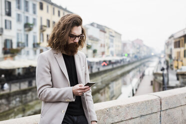 Stilvoller junger Mann im Freien, der sein Mobiltelefon überprüft - MAUF00931