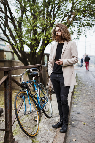 Stilvoller junger Mann im Freien mit Handy, der sich umschaut, lizenzfreies Stockfoto