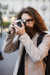 Stylish young man outdoors taking pictures with old-fashioned camera - MAUF00944