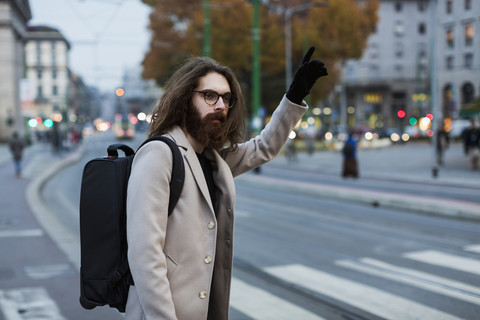 Stilvoller junger Mann in der Stadt, der ein Taxi ruft, lizenzfreies Stockfoto