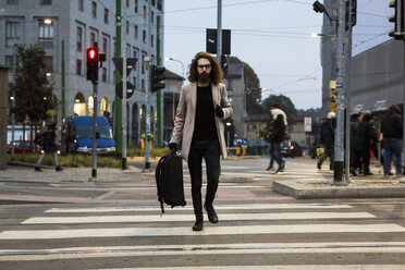 Stilvoller junger Mann mit Tasche, der die Straße auf einem Zebrastreifen überquert - MAUF00954