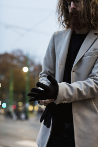 Stilvoller junger Mann im Freien, der Handschuhe anzieht, lizenzfreies Stockfoto