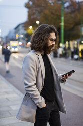 Stilvoller junger Mann in der Stadt, der sein Mobiltelefon überprüft - MAUF00960