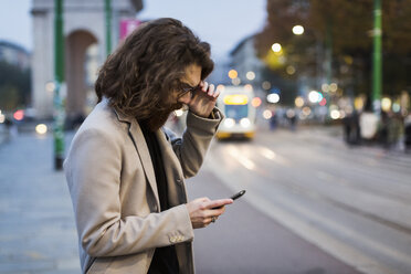 Stilvoller junger Mann in der Stadt, der sein Mobiltelefon überprüft - MAUF00962