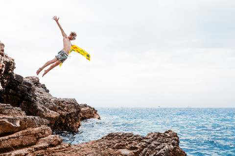 Man with airbed jumping from rock into the sea stock photo