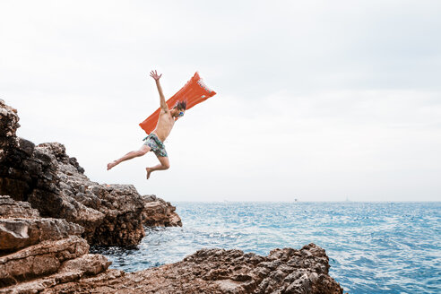 Mann mit Luftmatratze springt vom Felsen ins Meer - WVF00774