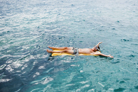 Glücklicher junger Mann entspannt sich auf einer Luftmatratze im Meer, lizenzfreies Stockfoto