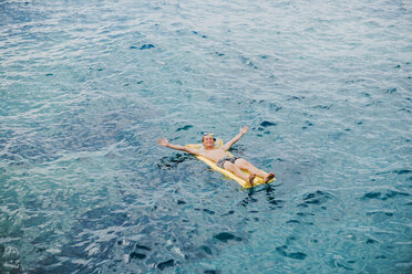 Glücklicher junger Mann entspannt sich auf einer Luftmatratze im Meer - WVF00776