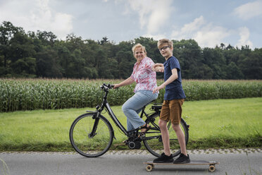 Grandson and grandmother riding bicycle and skateboard together - PAF01756