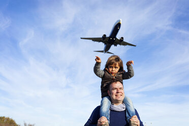 Father carrying son on shoulders under flying airplane - VABF01021