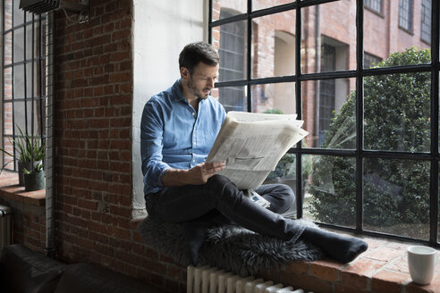 Älterer Mann sitzt auf der Fensterbank und liest Zeitung - RBF05549