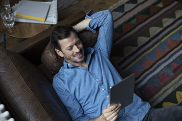Mann auf Couch liegend, mit digitalem Tablet - RBF05554