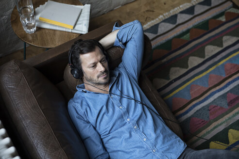 Mann auf Couch liegend, mit Kopfhörern - RBF05555
