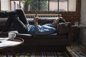 Mann liegt auf der Couch und benutzt ein Smartphone - RBF05556