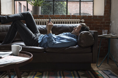 Man lying on couch, using smart phone - RBF05556