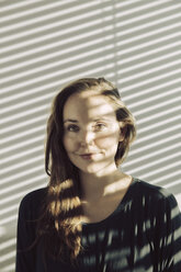 Portrait of smiling young woman sitting in a shadowed room - MFF03466