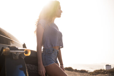 Young woman with skateboard leaning against car - SIPF01325