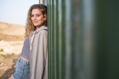 Porträt einer lächelnden jungen Frau, die sich an eine Wand lehnt, lizenzfreies Stockfoto