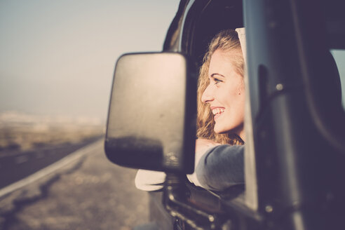 Glückliche junge Frau schaut aus dem Autofenster - SIPF01332