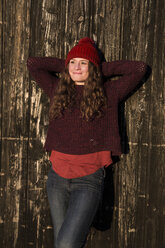 Portrait of relaxed young woman wearing winter fashion leaning against wooden wall - SARF03118