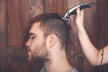 Junger Mann lässt sich von seiner Freundin die Haare mit einer Haarschneidemaschine schneiden - RTBF00587