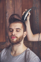 Porträt eines jungen Mannes, der sich von seiner Freundin mit einer Haarschneidemaschine die Haare schneiden lässt - RTBF00588