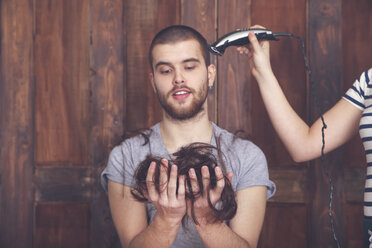 Porträt eines jungen Mannes, der sich von seiner Freundin mit einer Haarschneidemaschine die Haare schneiden lässt - RTBF00589