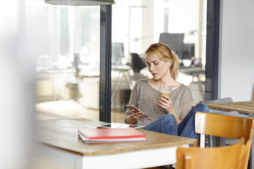 Frau überprüft Mobiltelefon im Büro - PESF00404