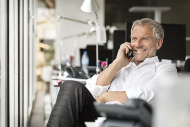 Lächelnder Geschäftsmann am Mobiltelefon im Büro - PESF00438