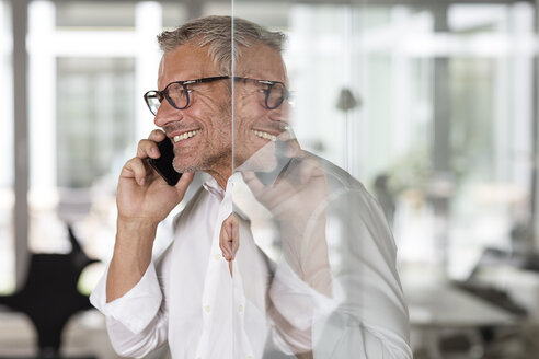 Lächelnder Geschäftsmann am Mobiltelefon im Büro - PESF00440