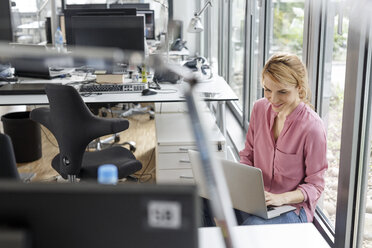 Smiling woman using laptop in office - PESF00446