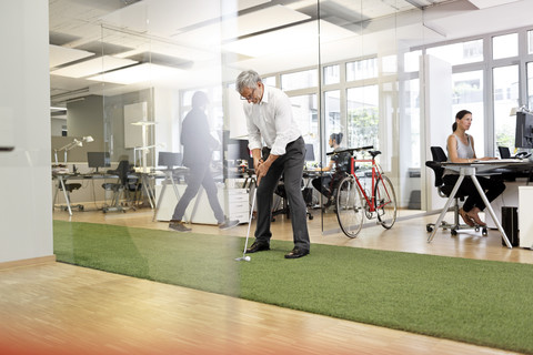 Businessman playing golf in office stock photo