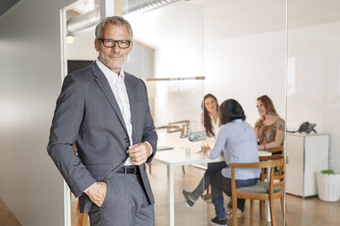 Confident businessman in office with employees in background - PESF00474