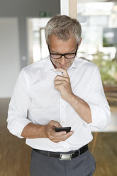 Businessman checking cell phone in office - PESF00476