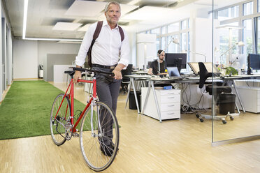 Geschäftsmann, der ein Fahrrad in einem modernen Büro schiebt - PESF00497