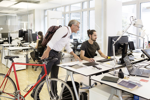 Geschäftsmann mit Fahrrad im Gespräch mit einem Kollegen in einem modernen Büro, lizenzfreies Stockfoto