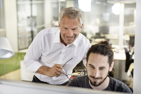 Zwei lächelnde Männer im Büro schauen auf einen Computerbildschirm - PESF00500