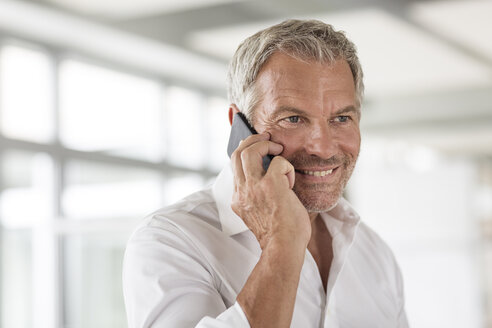 Lächelnder Geschäftsmann am Mobiltelefon im Büro - PESF00507