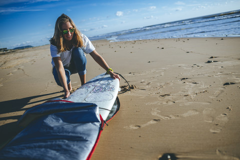 Junge Frau nimmt Surfbrett aus der Abdeckung am Strand, lizenzfreies Stockfoto