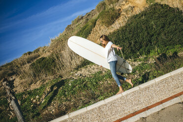 Junge Frau mit Surfbrett balanciert auf Wand - KIJF01084