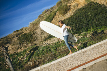 Young woman with surfboard balancing on wall - KIJF01084