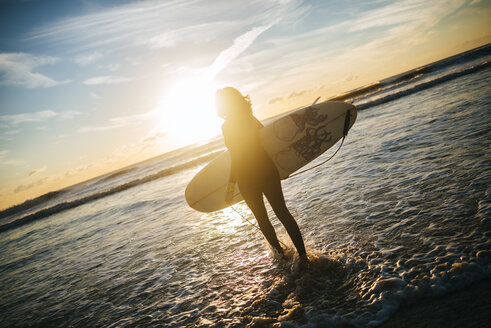 Frau mit Surfbrett geht bei Sonnenuntergang ins Meer - KIJF01098
