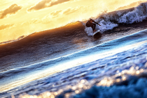 Junge Frau beim Surfen auf dem Meer bei Sonnenuntergang, lizenzfreies Stockfoto